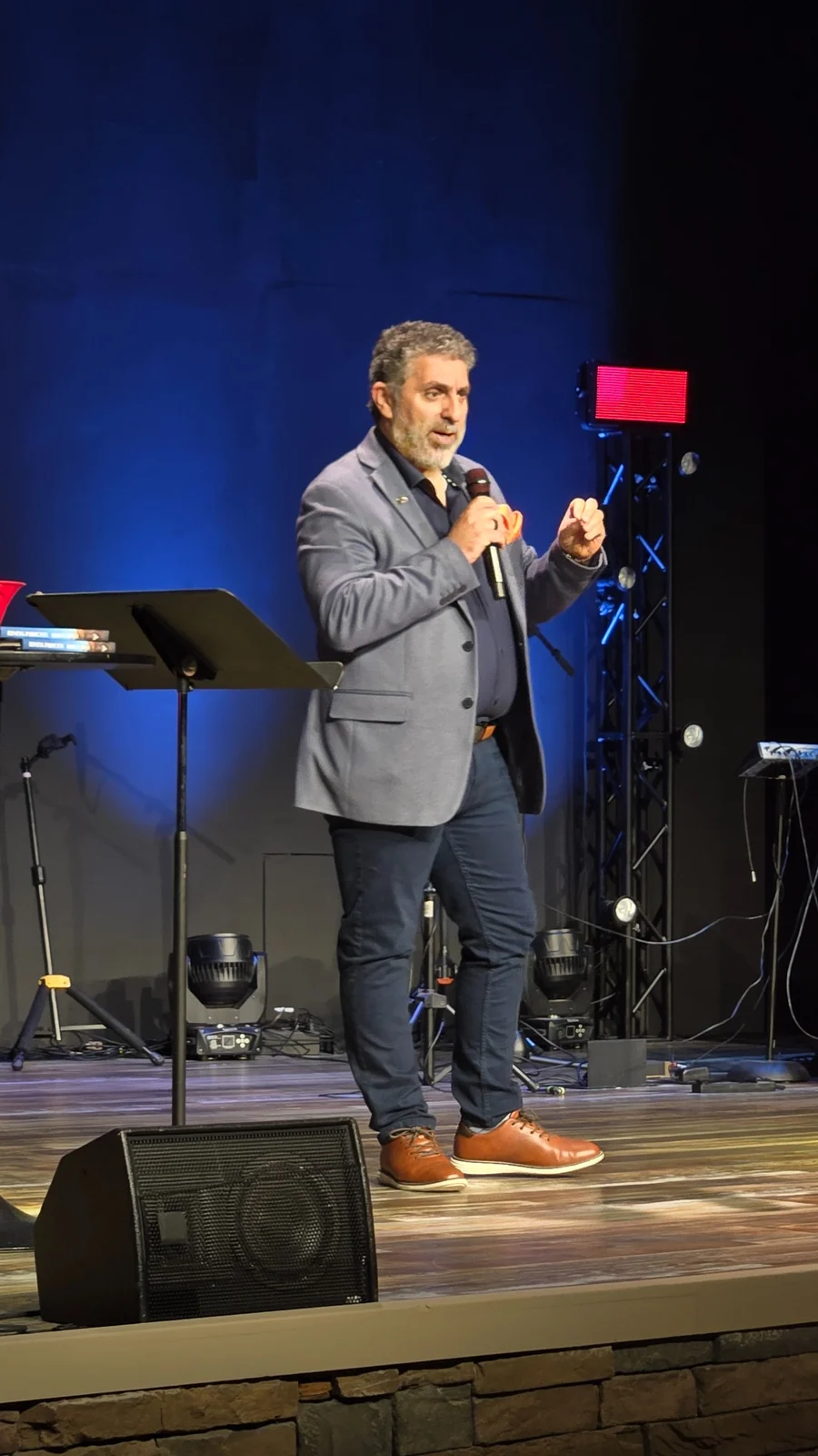 Romeo El Chaer speaking on stage with a handheld microphone
